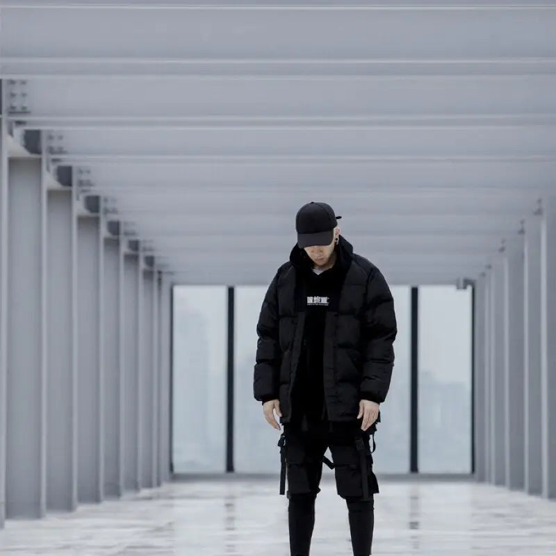 a man in a black jacket and pants stands in a long corridor